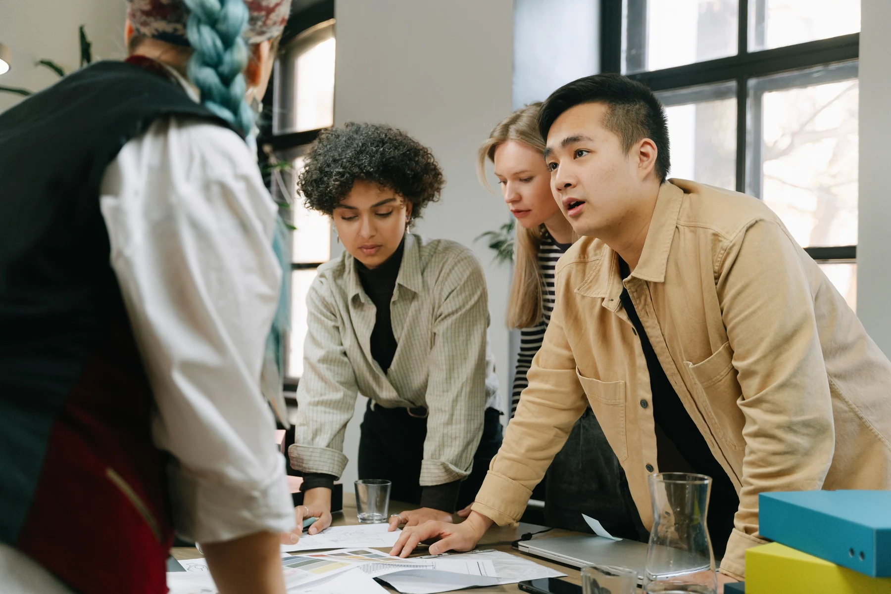 Four casually dressed coworkers reviewing documents together in a bright office